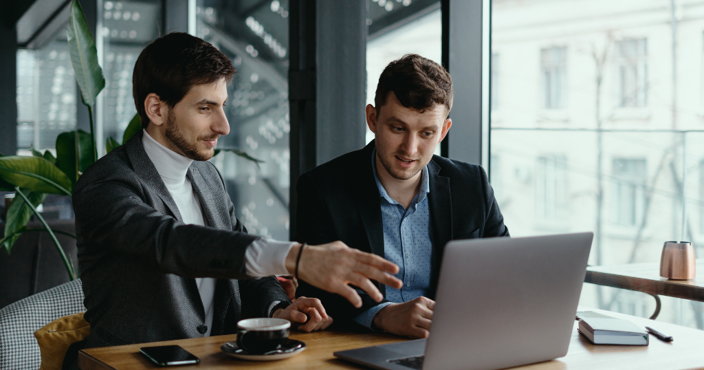 Two business consultants in formal attire discussing strategies while working on a laptop at a modern cafe. Top Business Consultants in UK.