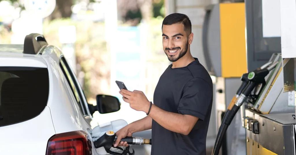 A smiling customer refueling his car while using his phone at a petrol station in Birmingham.