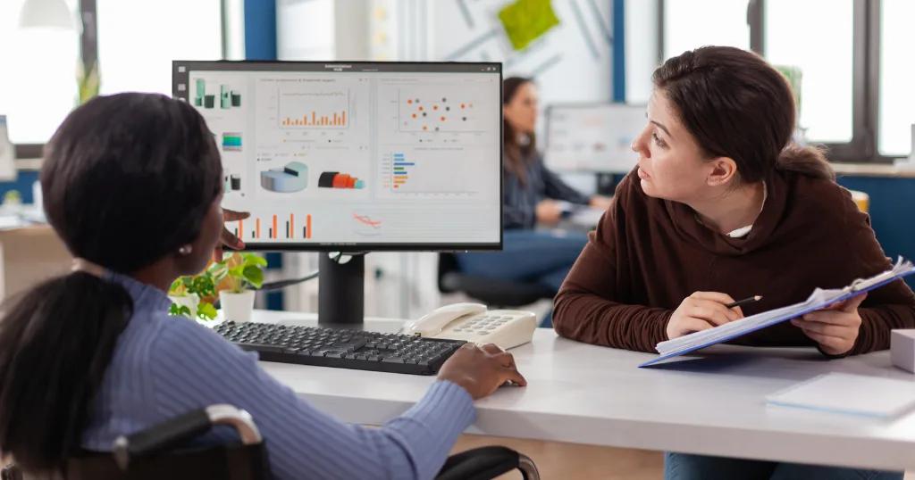 Two professionals discussing graphs and data analytics on a computer screen in an office environment, focusing on AI-Driven SEO strategies.