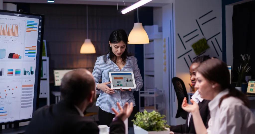 A businesswoman presenting AI-powered digital marketing strategies using a tablet in a modern office meeting room.