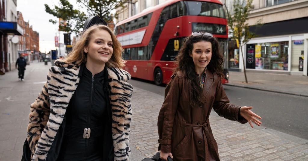 Two women walking by a red bus in London, related to UK Visa Services Lahore.