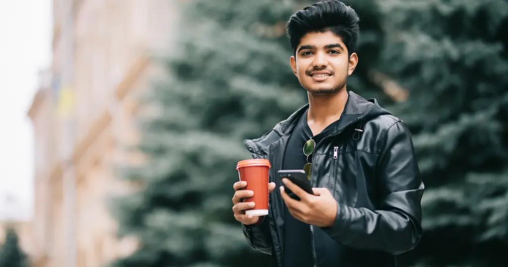 A young man with coffee and a phone enjoying his time outdoors. UK Visit Visa from Pakistan offers exciting travel experiences.