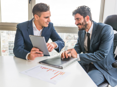 Two business consultants reviewing financial charts on a tablet in a corporate office. Top Business Consultants in UK.