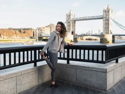 A woman stretching near Tower Bridge, ready for her UK Visa adventure in London.